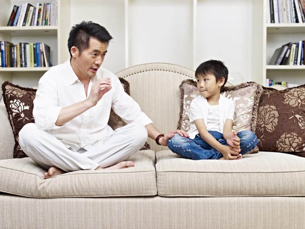 father and son having a conversation on couch at home.